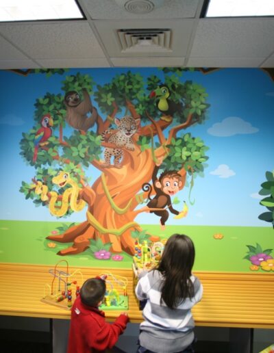 Children interact with colorful jungle-themed decor featuring a large tree and playful animals.